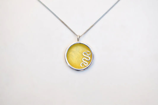 A silver chain necklace with a round pendant featuring a textured yellow center and a white snake design, displayed on a clean white background.