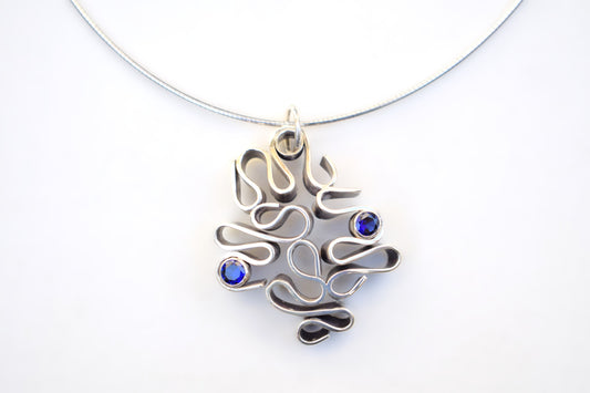 A silver-toned abstract pendant necklace with three small round blue gemstones, shown on a plain white background.