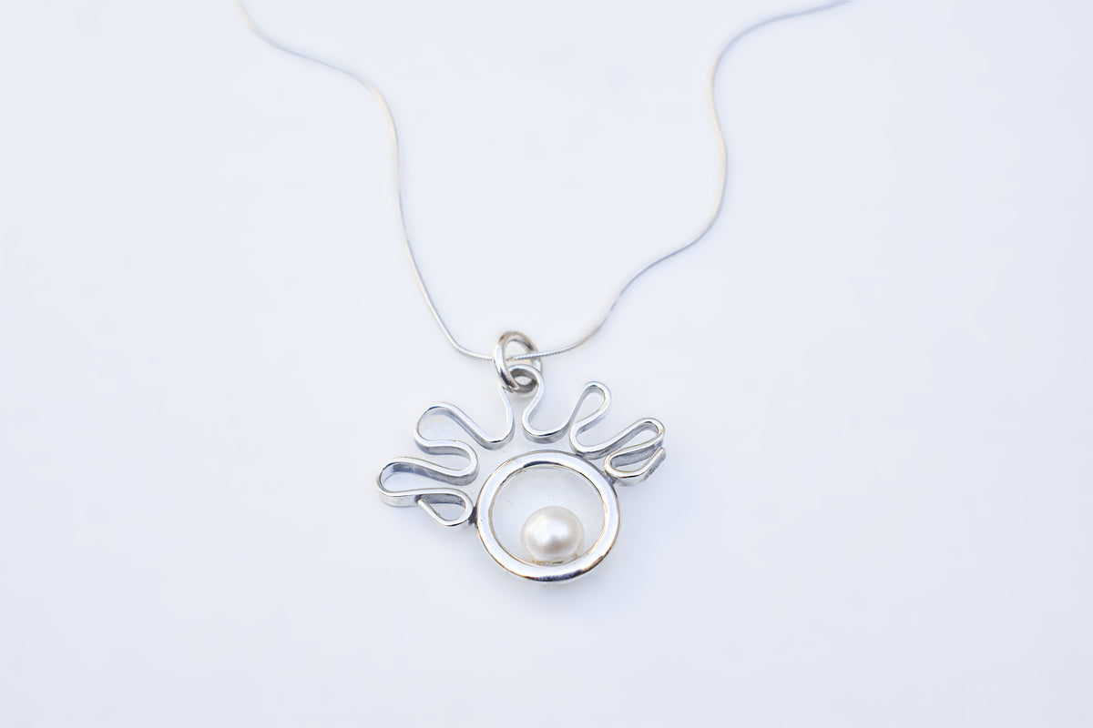 A silver pendant necklace featuring a circular silver frame with a white pearl nestled in the center, suspended from a delicate silver chain against a plain white background.