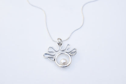 A silver pendant necklace featuring a circular silver frame with a white pearl nestled in the center, suspended from a delicate silver chain against a plain white background.