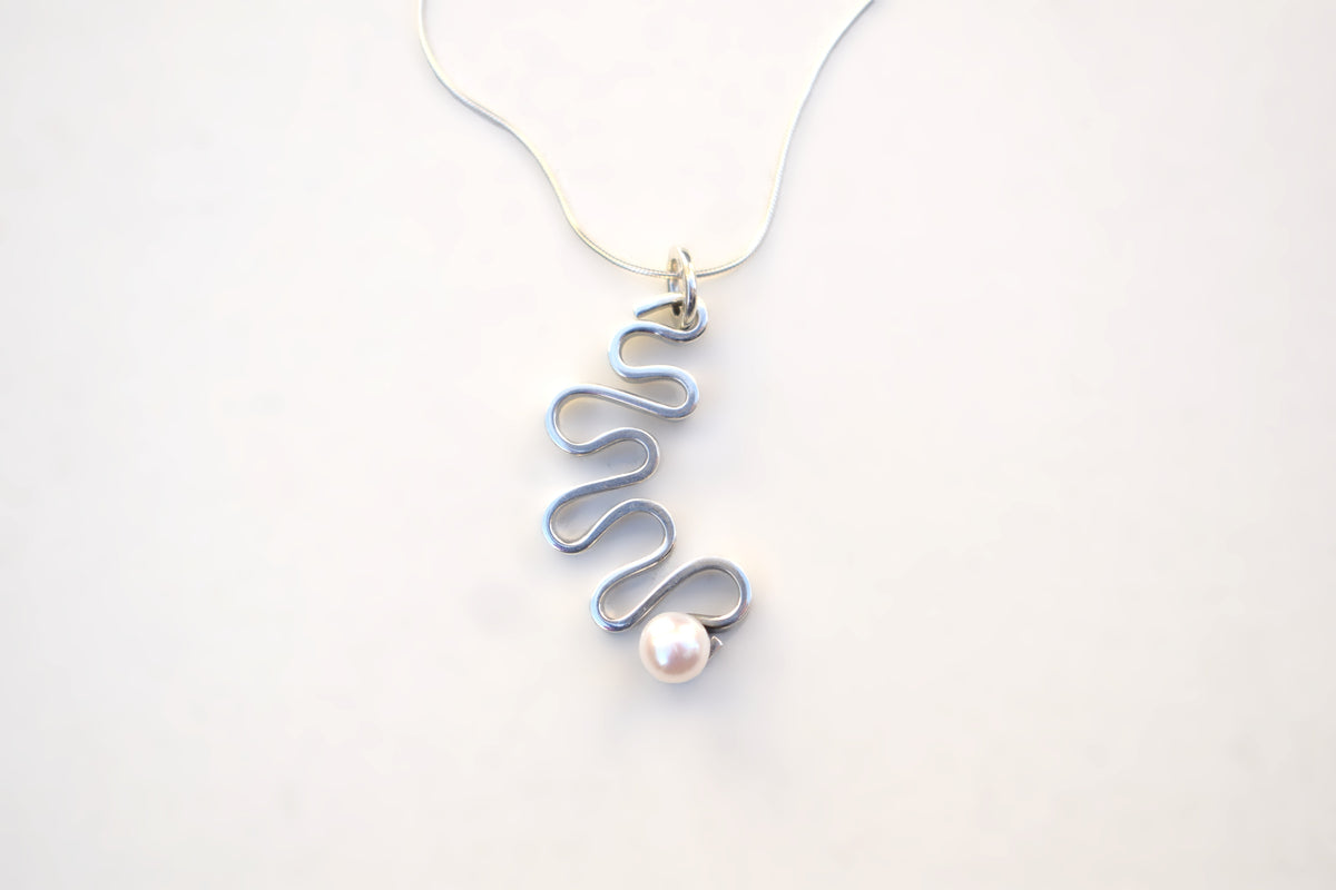 A silver wavy spiral pendant necklace with a single white pearl, shown on a thin silver chain against a plain white background.