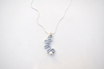 A delicate silver wire pendant necklace with a wavy, coiled design and a small white pearl accent, displayed on a clean white background.