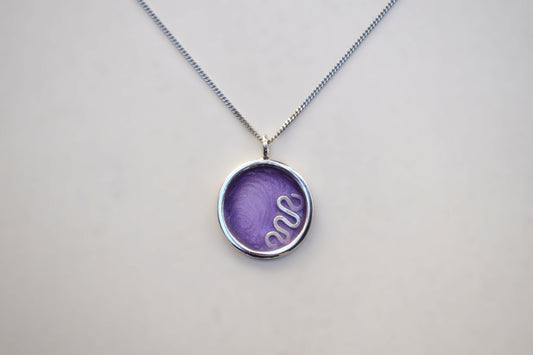 A silver chain necklace with a round bezel pendant containing a purple textured insert with a white snake design, shown on a light gray background.