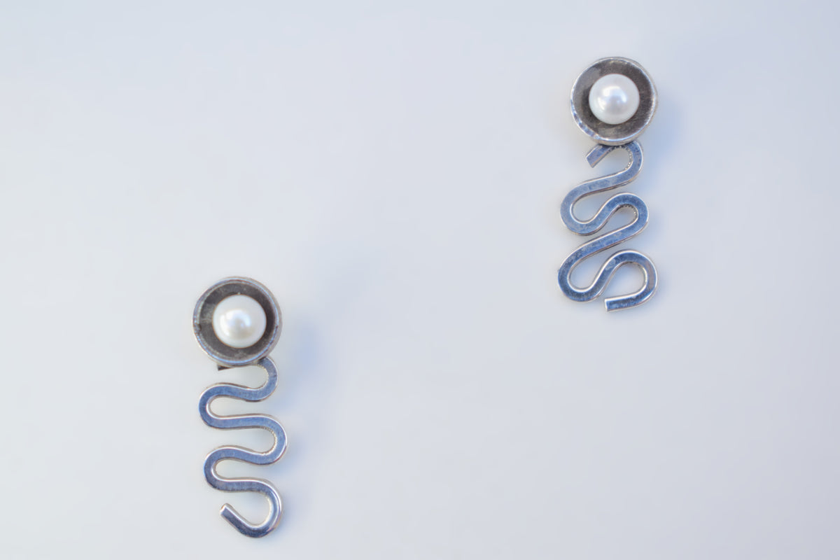 A pair of silver-toned spring earrings with a small white pearl at the top, displayed on a clean white background.