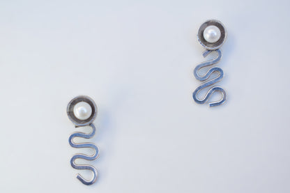 A pair of silver-toned spring earrings with a small white pearl at the top, displayed on a clean white background.