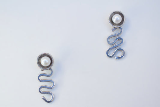 A pair of silver-toned spring earrings with a small white pearl at the top, displayed on a clean white background.