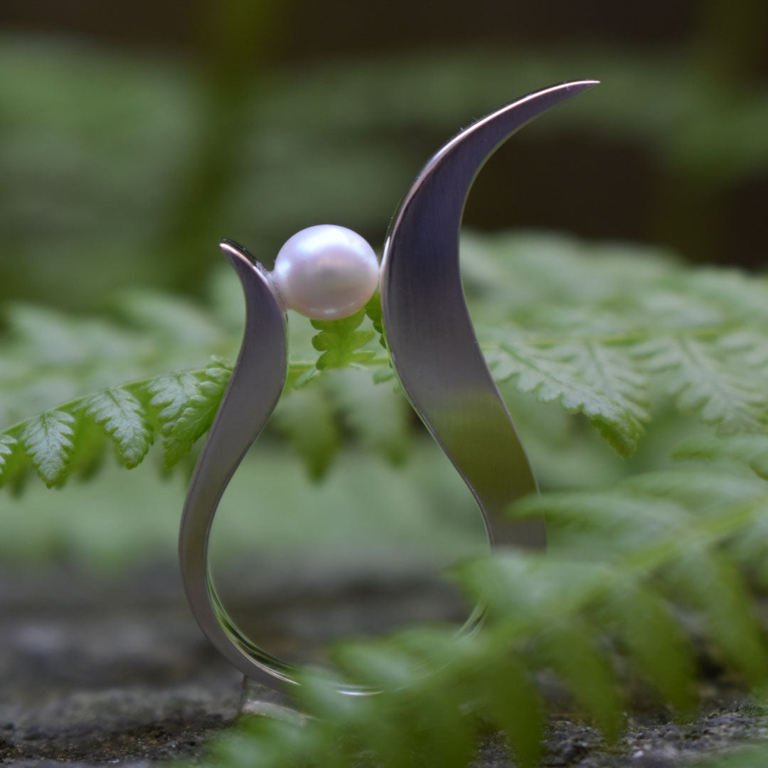 Elegant sterling silver ring with a lustrous pearl, designed to resemble delicate leaves, photographed against a natural green fern background.